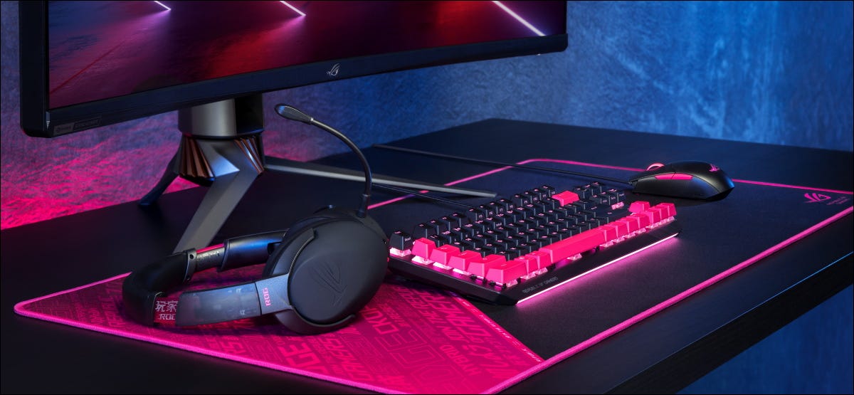 Teclado iluminado por LED de um PC para jogos, fones de ouvido, mouse e visor em uma mesa.