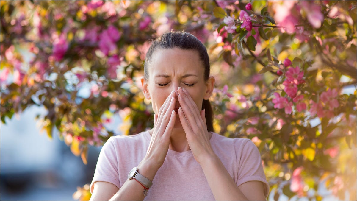 Mulher em pé sob uma árvore espirrando de alergia a pólen