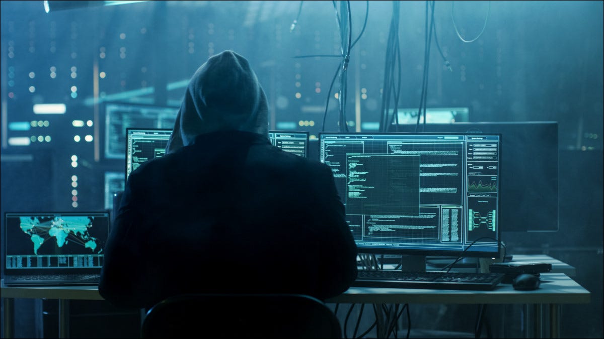 Um hacker encapuzado sentado na frente de computadores.