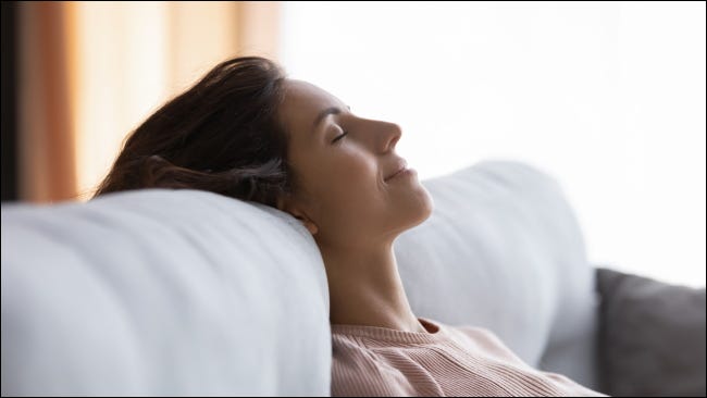 Uma mulher relaxando em seu sofá com os olhos fechados.