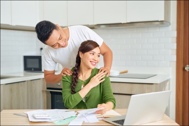 Um homem massageando os ombros de sua esposa em uma cozinha.