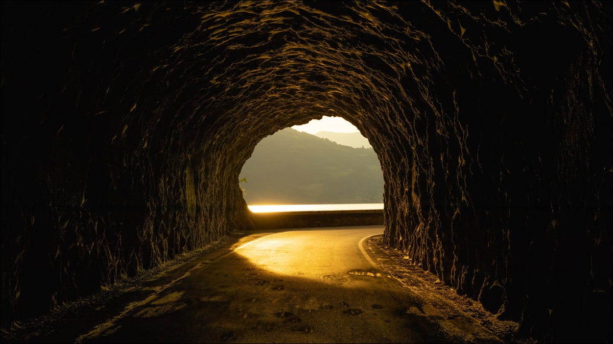 Um túnel rochoso com um pôr do sol do outro lado.