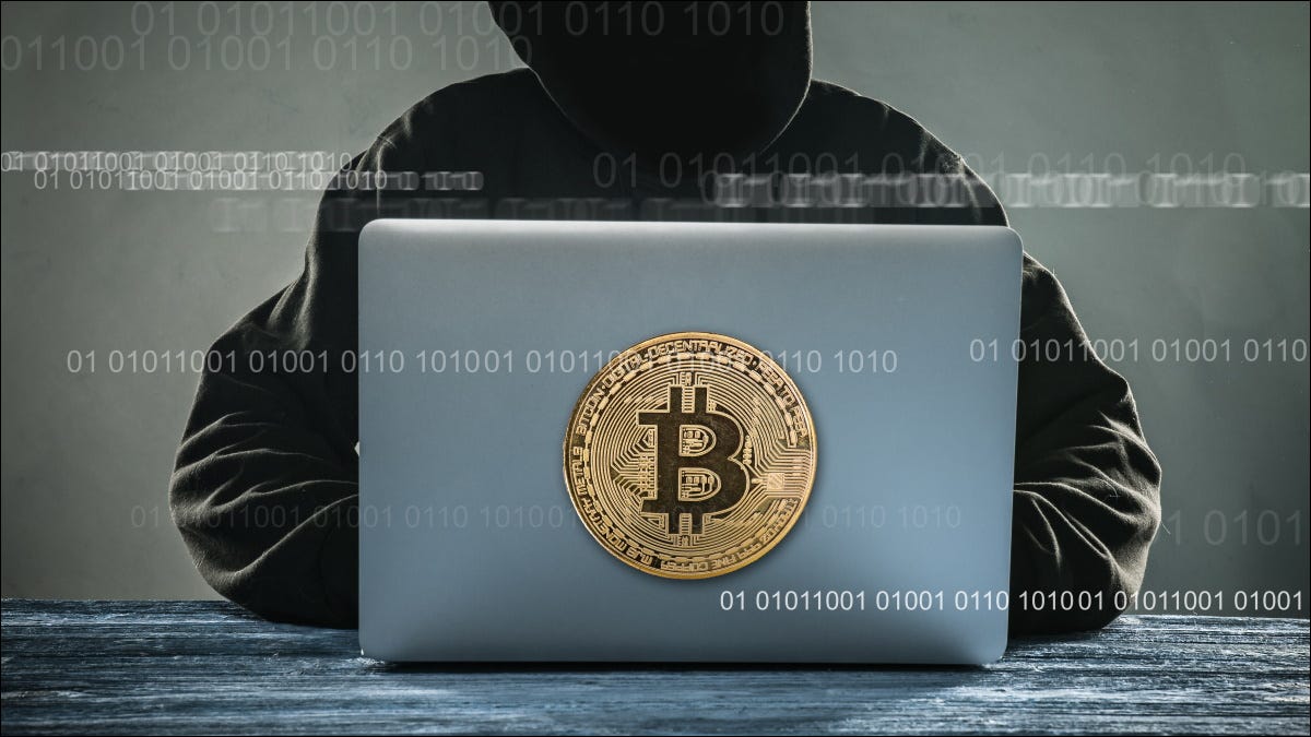 Um estilizado "hacker" anônimo usando um laptop com uma ilustração de Bitcoin.