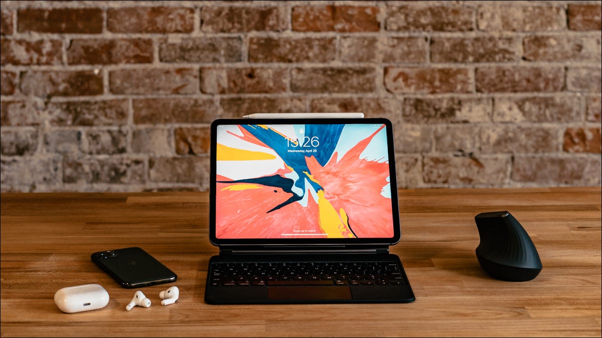 iPad em uma mesa com teclado Magic, iPhone, AirPods e mouse de computador