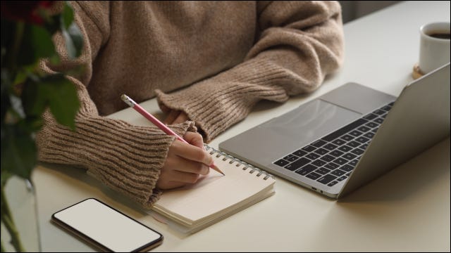 Mulher fazendo anotações em papel ao lado de um laptop