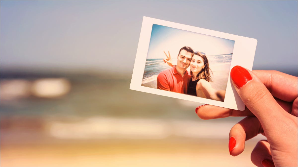 Mão de uma mulher segurando uma foto de casal em frente à praia