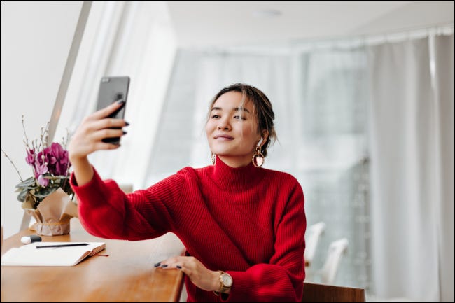 Mulher com um suéter vermelho tirando uma selfie sob a luz natural de uma janela