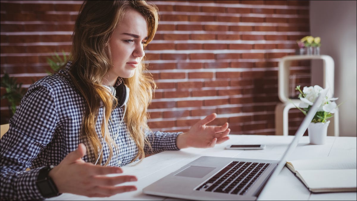 Mulher jovem com as mãos ao alto em frustração com um laptop Macbook