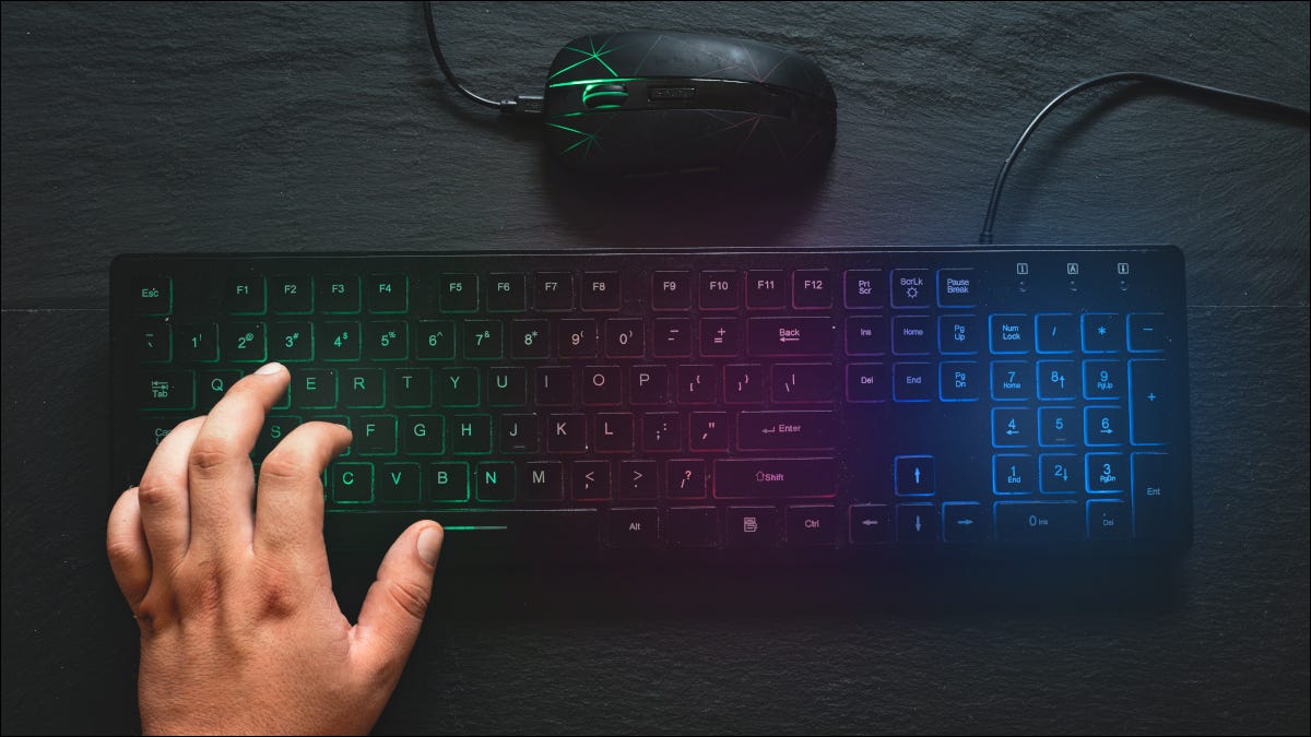 Teclado colorido RGB e mouse com a mão no teclado
