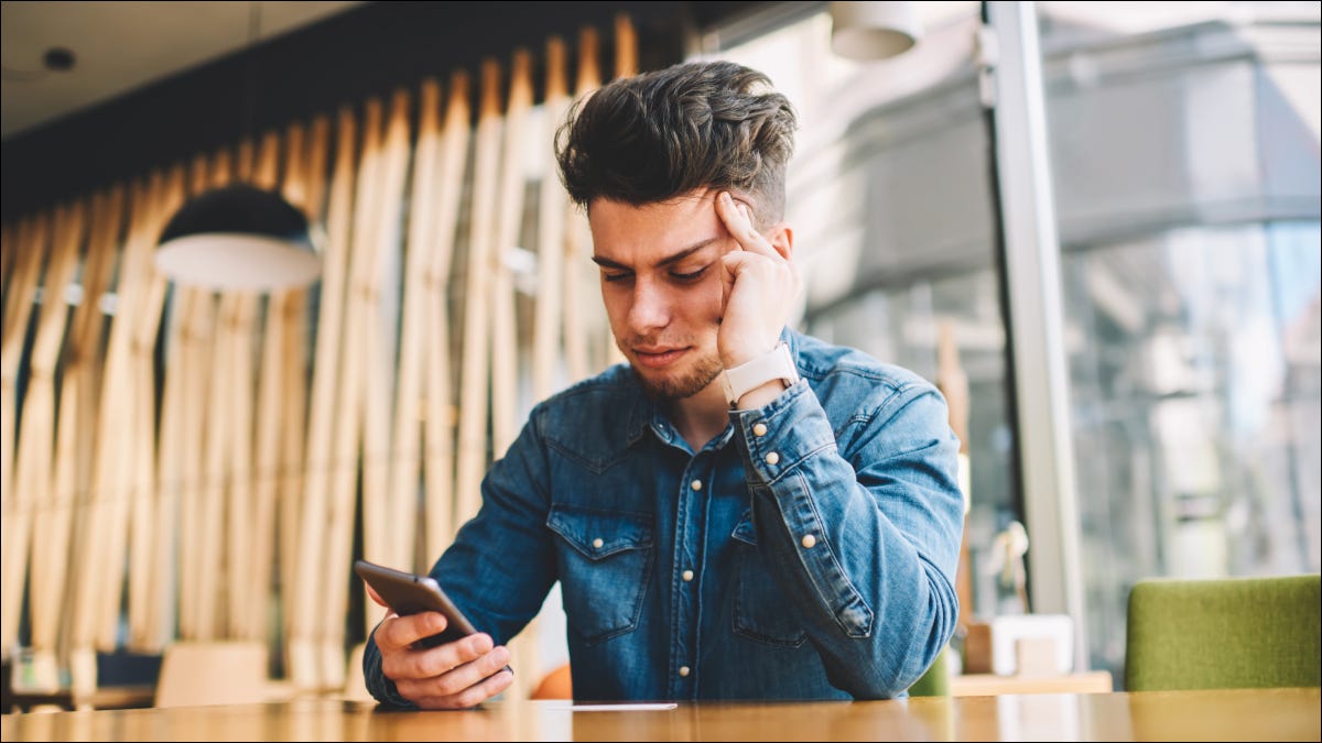 Homem olhando para o telefone com expressão estressada.