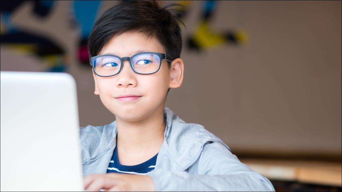 Menino pré-adolescente de óculos em um laptop sorrindo e revirando os olhos