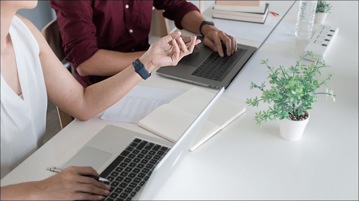 Duas pessoas usando dois laptops em uma mesa.