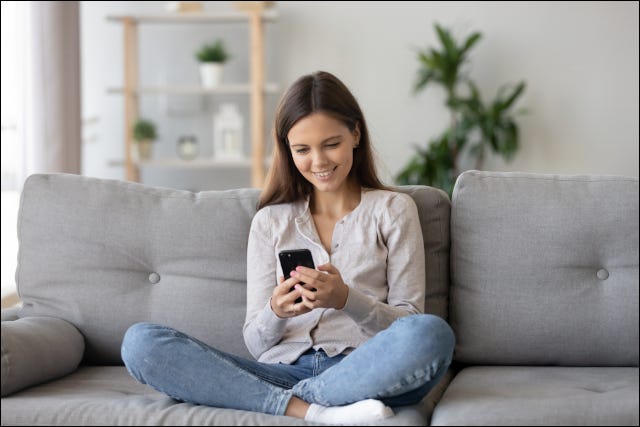 Adolescente sorrindo e sentada no sofá com o smartphone