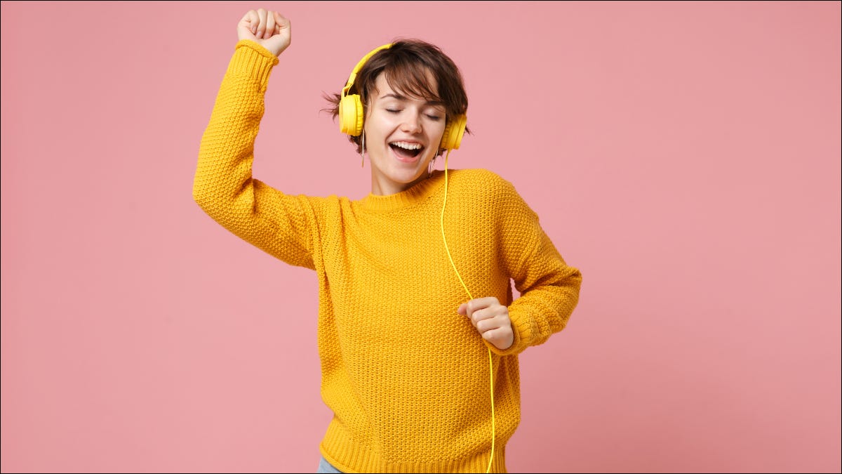 Mulher com suéter amarelo dançando enquanto ouve música em fones de ouvido amarelos com fio
