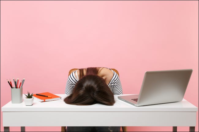 Mulher exausta com o rosto plantado na mesa ao lado do computador e material de escritório.