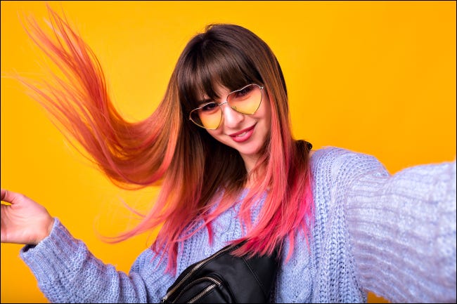 Mulher jovem tirando uma selfie com cabelo rosa contra um fundo amarelo no ar