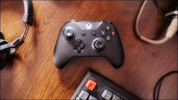 Controlador do Xbox One com fone de ouvido e teclado na superfície de madeira.