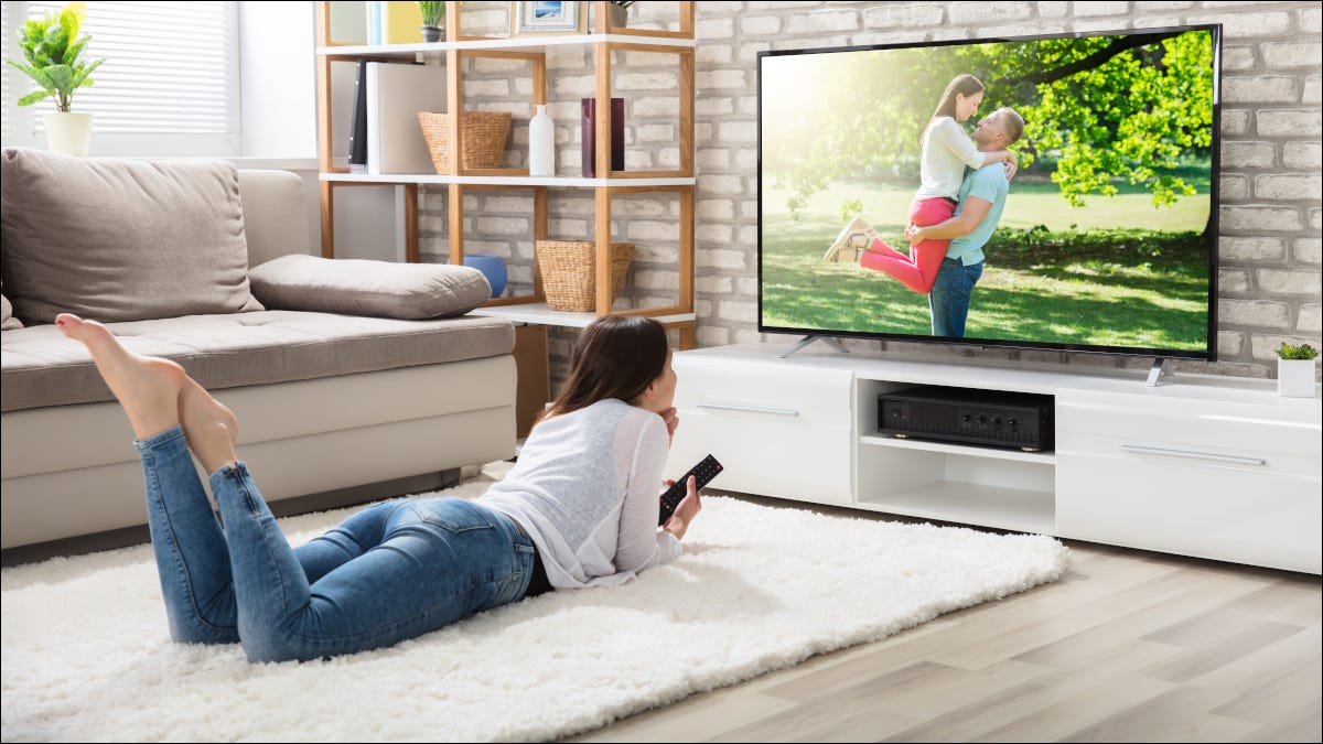 Mulher jovem deitada no chão assistindo TV