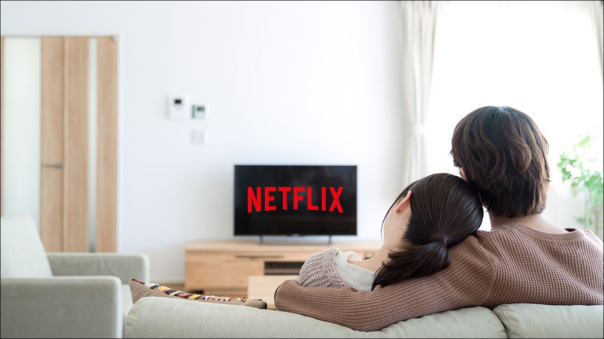 Casal sentado em um sofá assistindo Netflix na TV