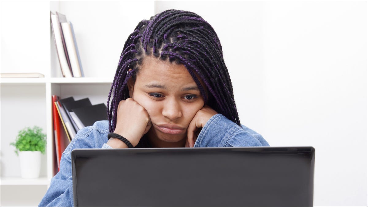 Mulher olhando para uma tela de laptop com uma expressão cansada no rosto.