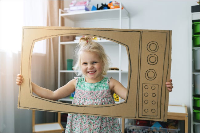 Criança sorridente dentro de um aparelho de TV de papelão