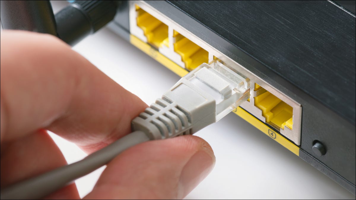 Close de uma mão humana conectando um cabo Ethernet a um roteador