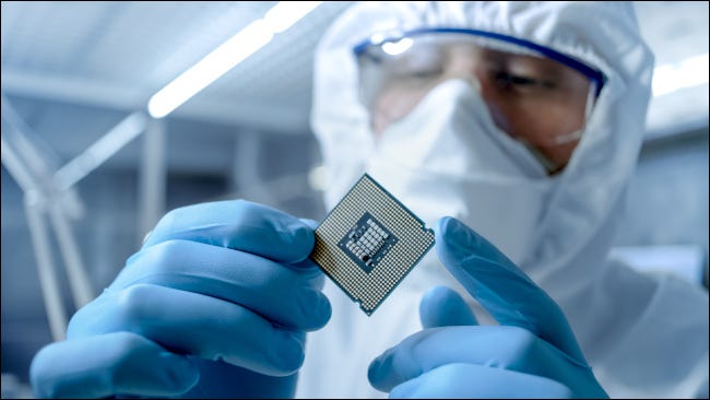 Homem em traje esterilizado examinando um microchip em uma fábrica