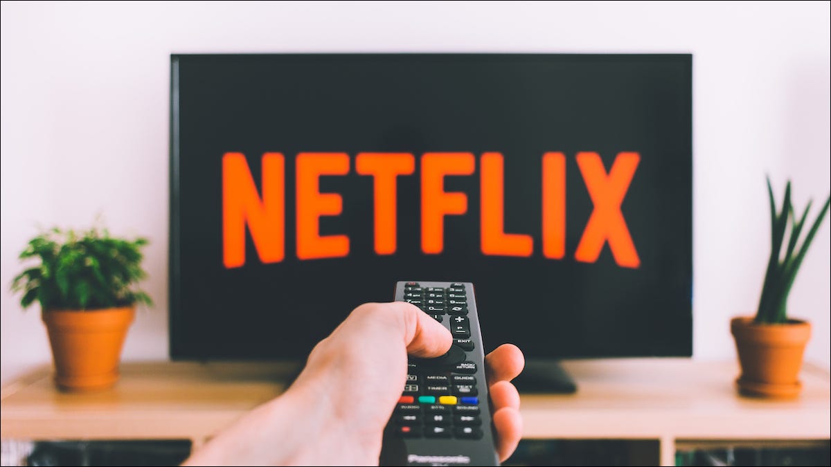 Pessoa apontando um controle remoto em direção a uma TV com o logotipo da Netflix