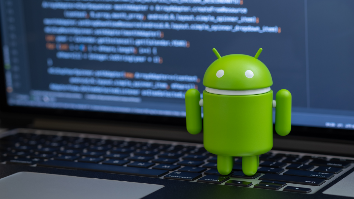 Estatueta da mascote Android em pé sobre um teclado de laptop