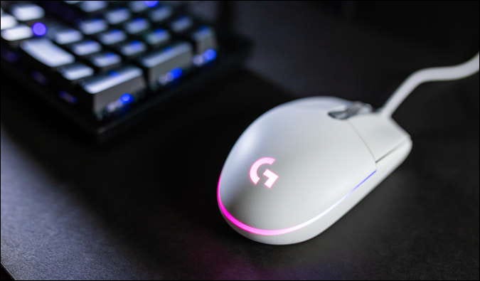 mouse logitech rgb branco em dekstop preto, com teclado em segundo plano