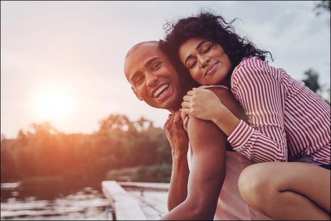 Um casal se abraçando e parecendo feliz na doca de um lago