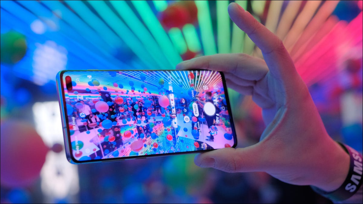 Mão segurando um Samsung Galaxy S10 com uma tela coloful na frente de luzes multicoloridas.