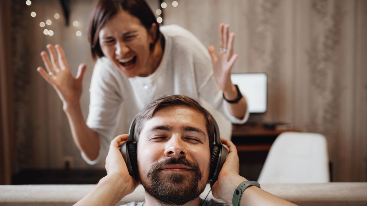 Homem usando fones de ouvido com um sorriso enquanto uma mulher grita de raiva.