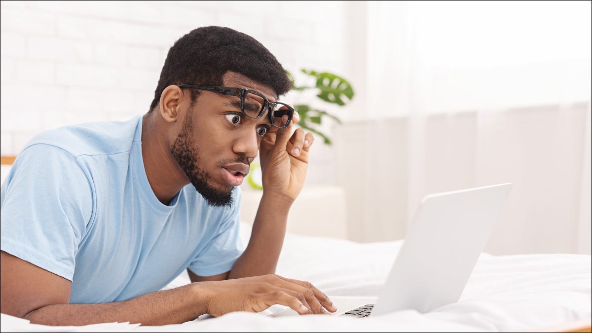 Homem levantando óculos e olhando chocado para a tela de um laptop