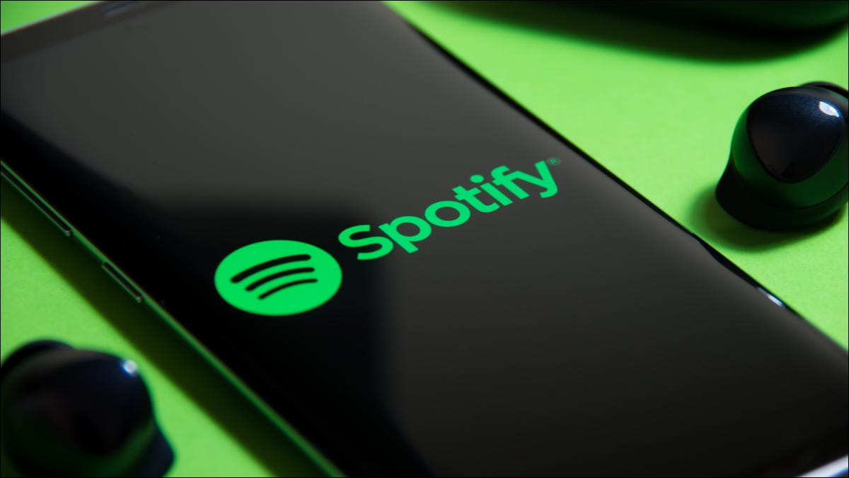 Smartphone mostrando o logotipo do Spotify ao lado de fones de ouvido sem fio em um fundo verde.