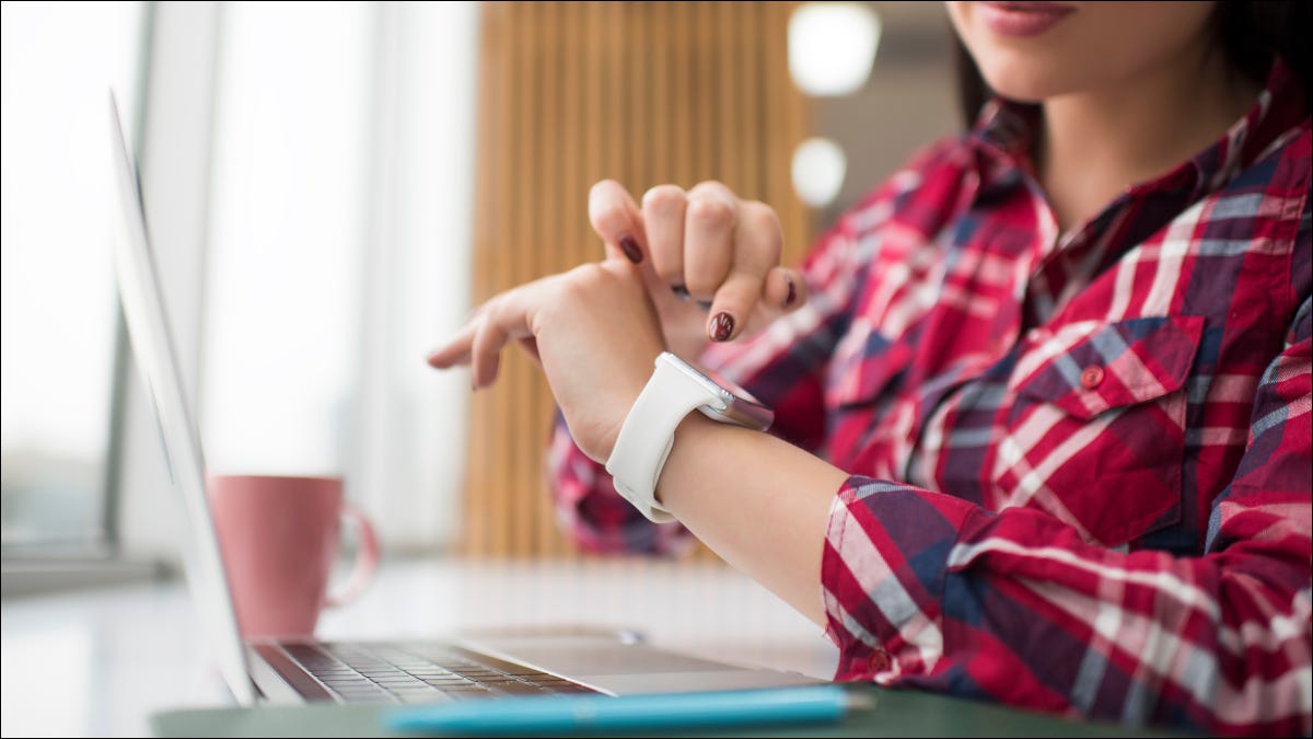 Mulher olhando para smartwatch enquanto usa um laptop