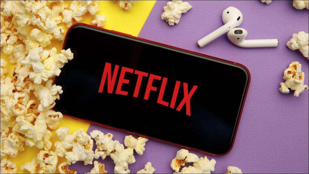 Logotipo da Netflix em um iPhone e ao lado de AirPods e pipoca