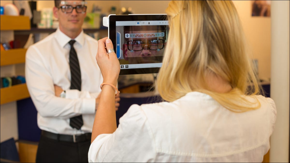 Um optometrista medindo a distância do olho de um homem com um tablet e uma câmera.