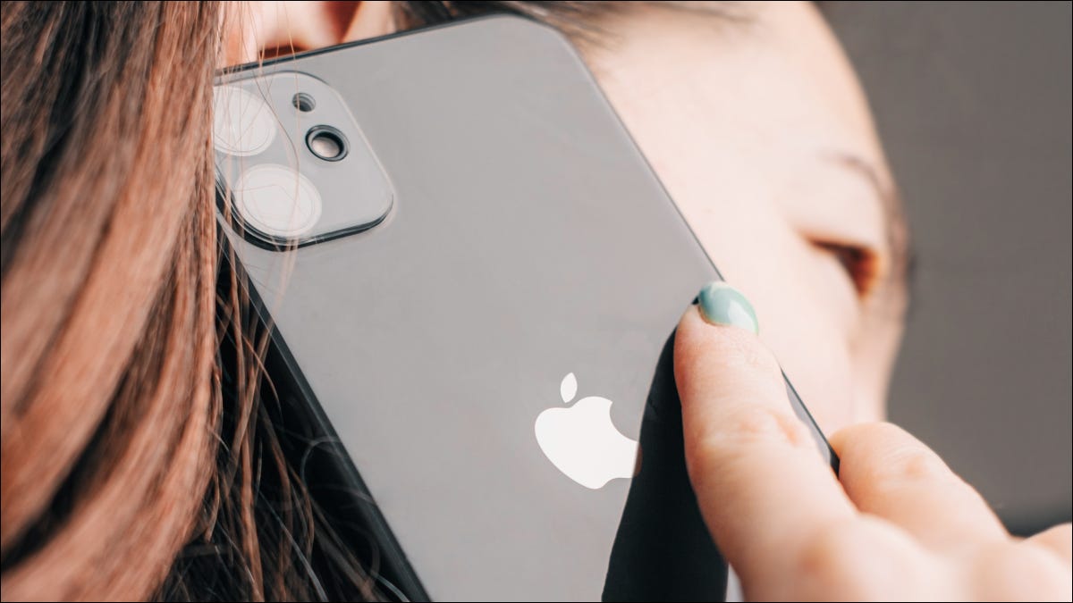 Close de um iPhone 11 preto pressionado contra a orelha de uma mulher