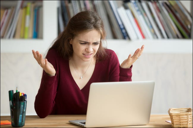 Mulher olhando para o laptop com uma expressão frustrada e as mãos no ar