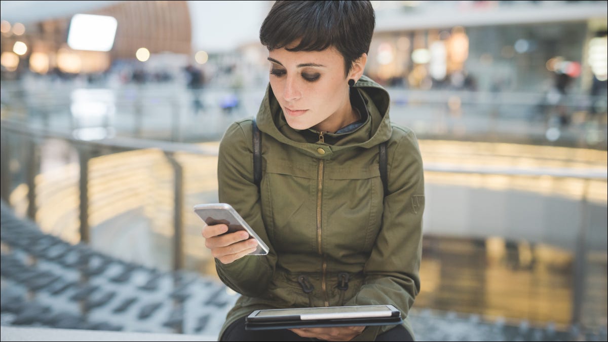 Mulher olhando para um smartphone com uma mão, enquanto segura o tablet com a outra.