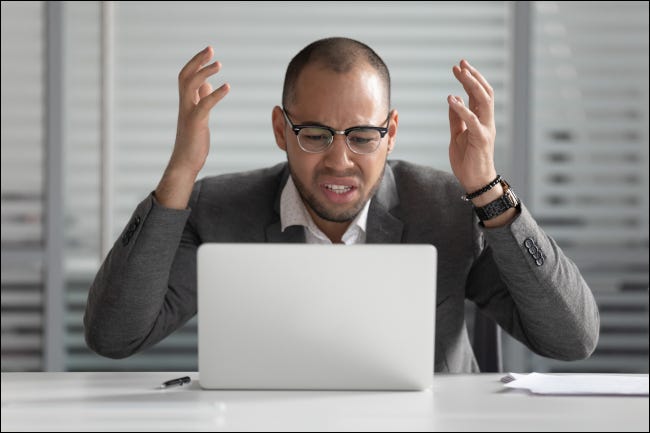 Empresário olhando para uma tela de laptop com uma expressão frustrada ou indignada.