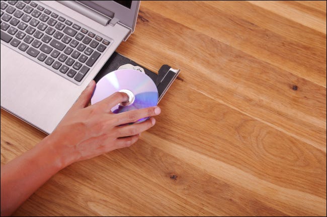 Mão colocando um CD na unidade de disco de um laptop
