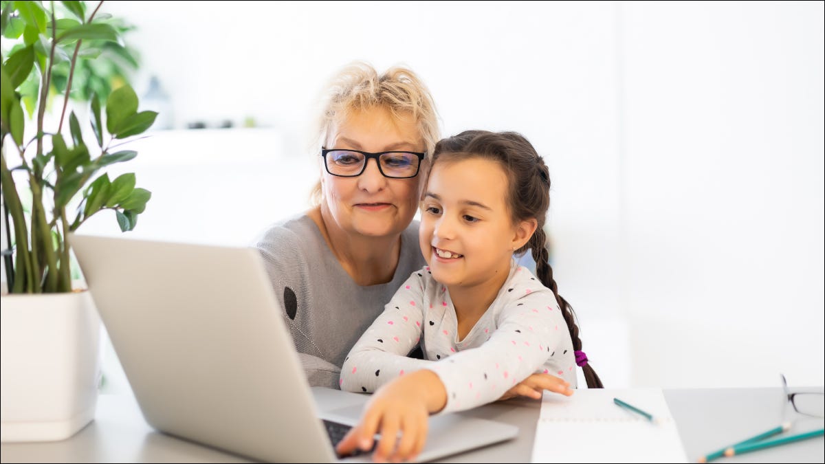 Uma mulher ajuda uma criança a usar um laptop.