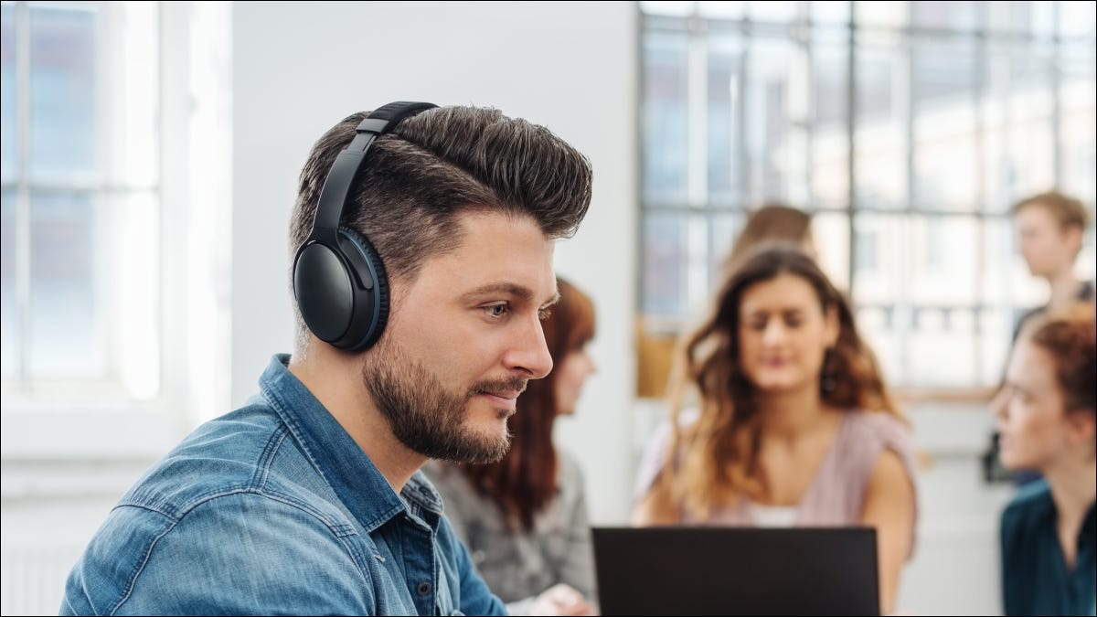 Homem usando fones de ouvido em um escritório ocupado.