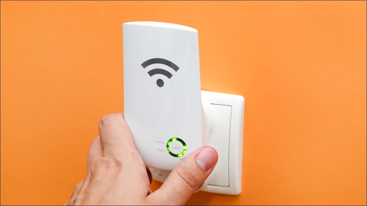 Uma mão segurando um repetidor Wi-Fi em uma tomada elétrica.