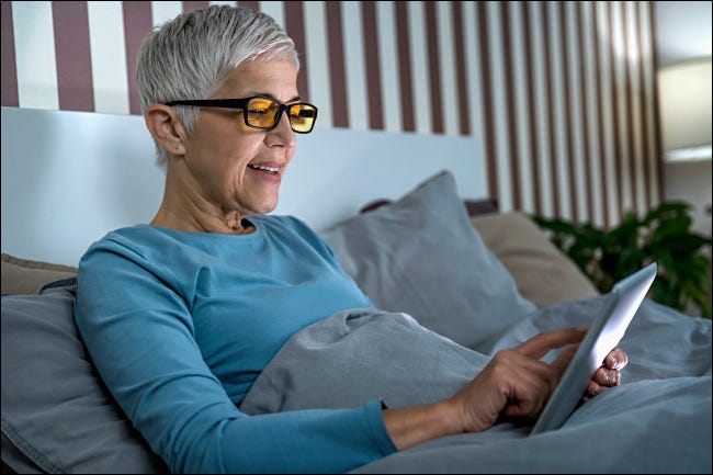 Uma mulher usando óculos bloqueadores de luz azul na cama.