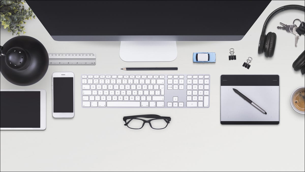 Uma mesa de escritório com computador, smartphone com teclado, fones de ouvido e muito mais