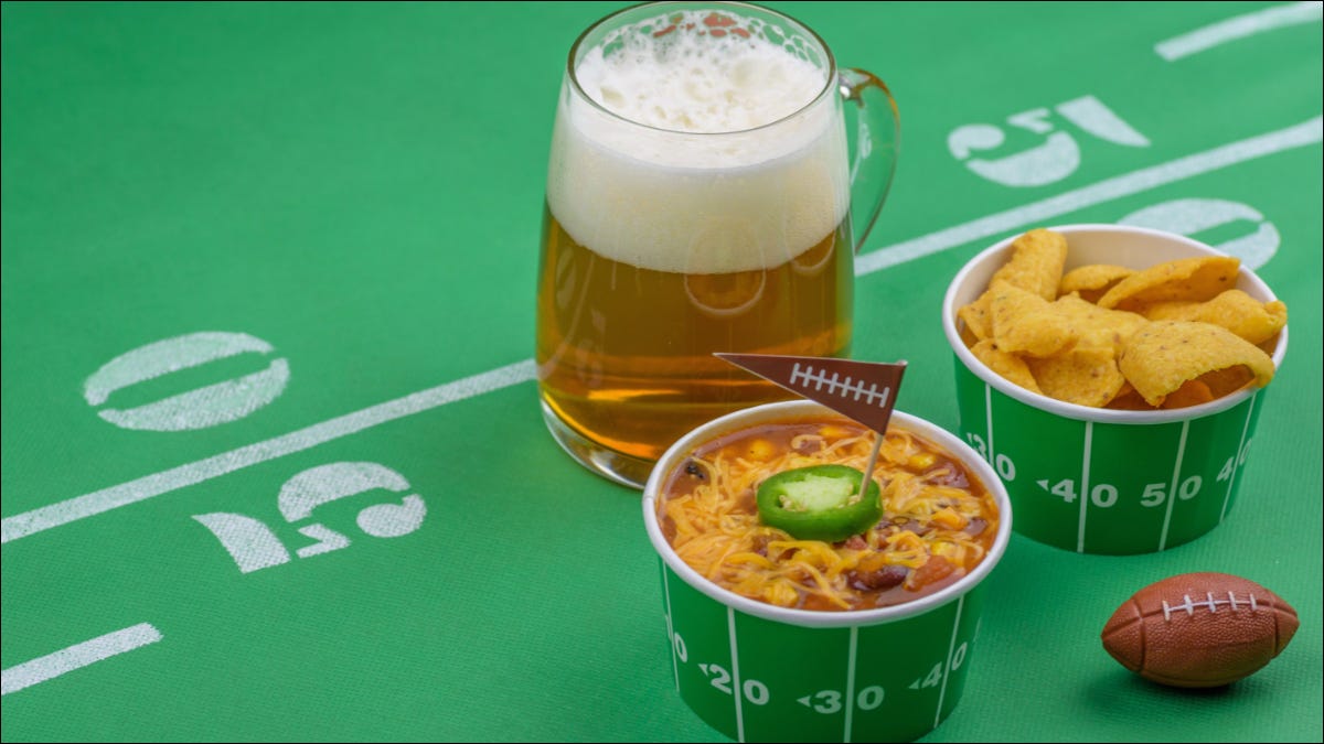 Mesa com tema de futebol com tigelas de chili com tema de futebol e um copo de cerveja