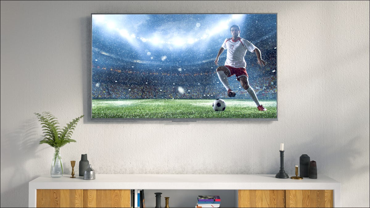 Uma TV LED pendurada na parede de uma sala de estar, com um jogador de futebol na tela.